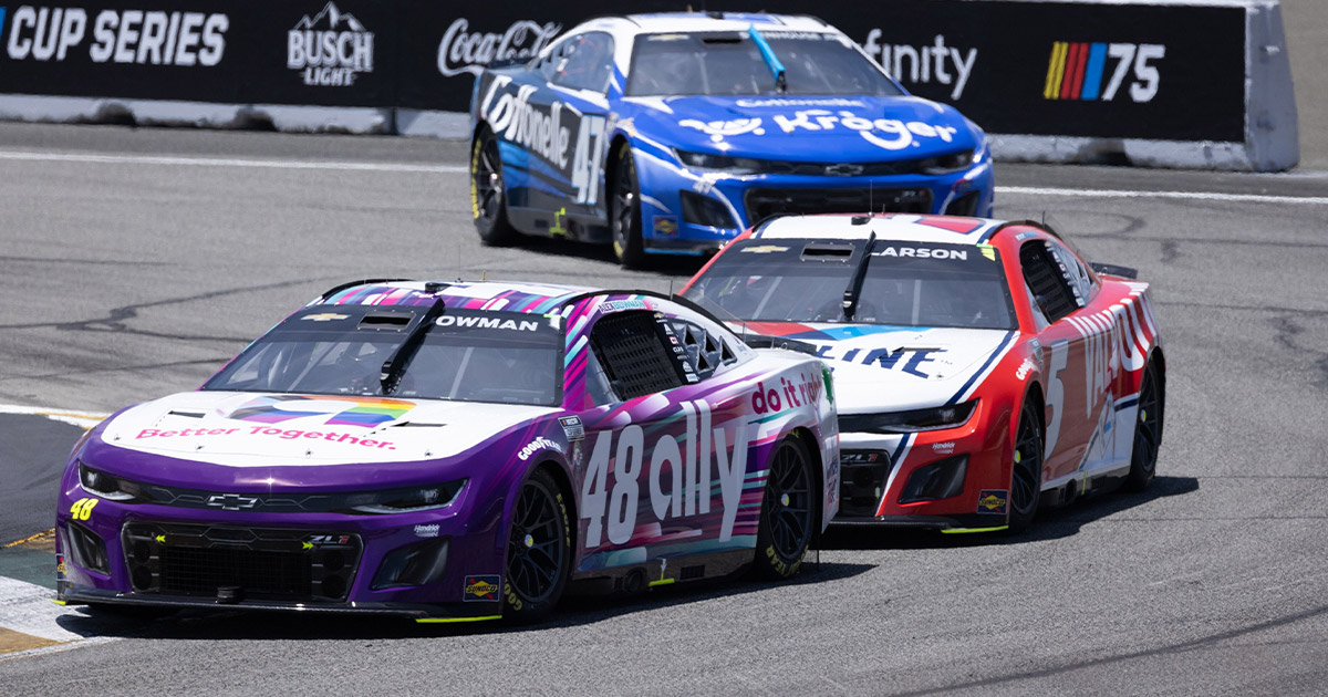 Three NASCAR race cars speed around a track. The leading car is purple with "48 Ally" branding, followed by a red car and a blue car.